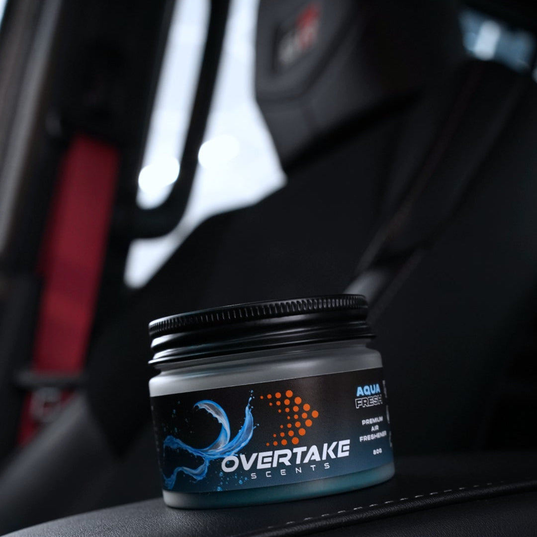 Aqua Fresh gel car air freshener on black leather car surface, red racing harness visible in background — Overtake Scents
