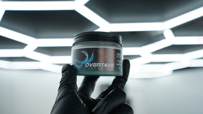 Aqua Fresh gel car air freshener held in black-gloved hand at car detailing studio with hexagonal ceiling lights — Overtake Scents