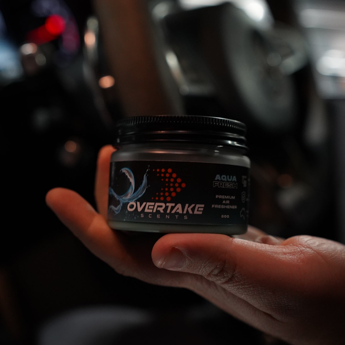 Aqua Fresh gel car air freshener resting in open palm, dark moody garage setting — Overtake Scents
