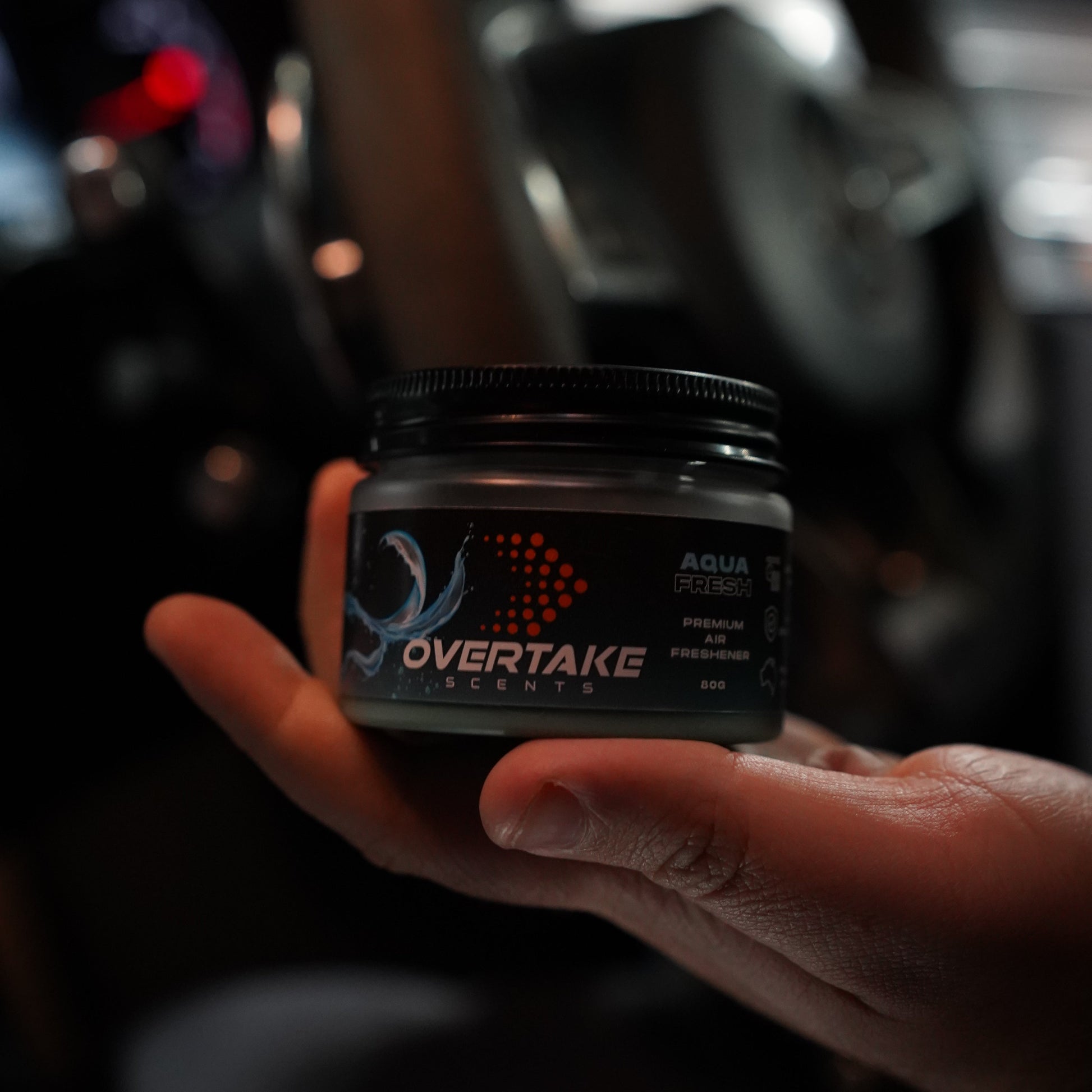 Aqua Fresh gel car air freshener resting in open palm, dark moody garage setting — Overtake Scents