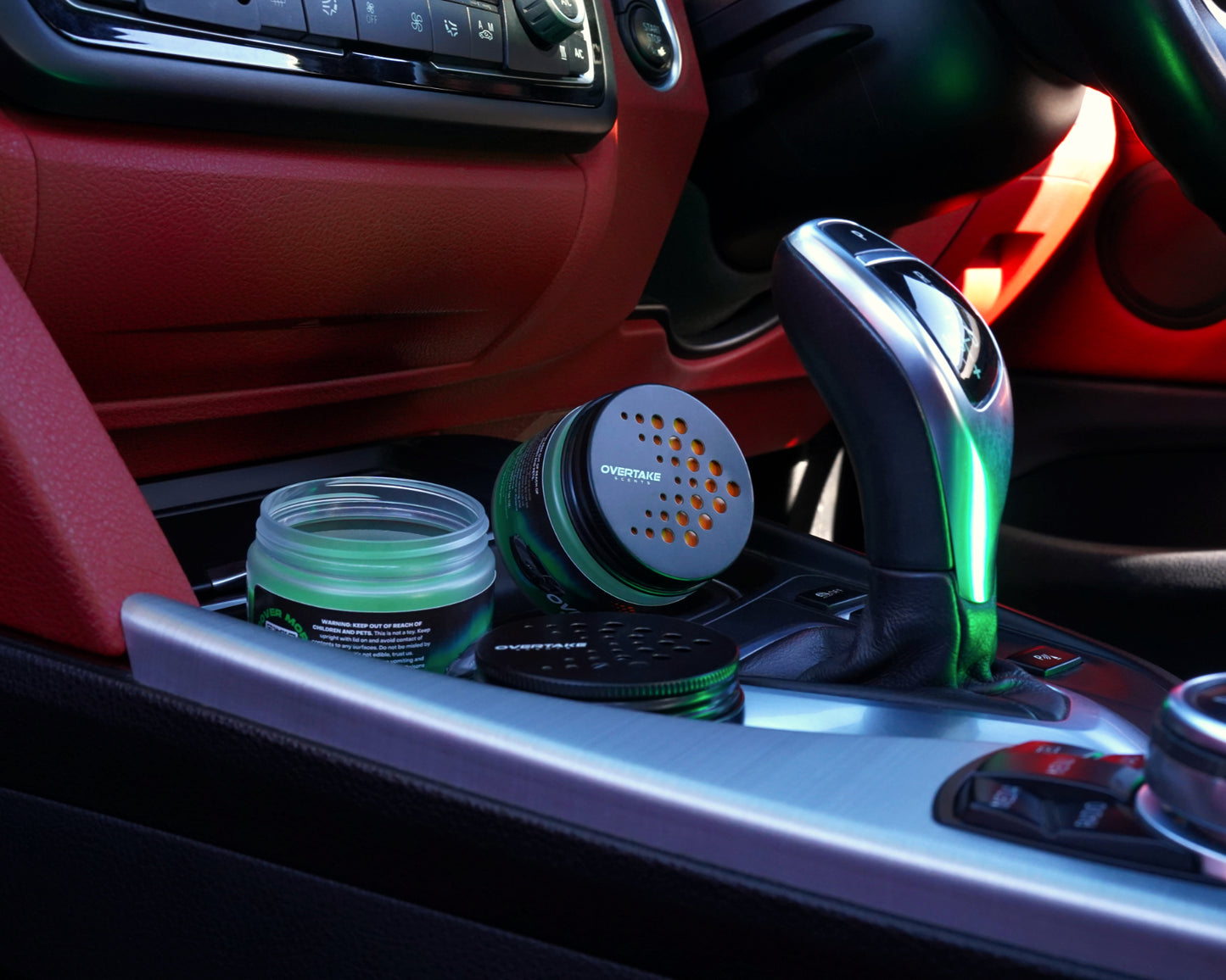 Auto Aurora gel car air freshener open in car center console with red leather interior and green ambient glow — Overtake Scents