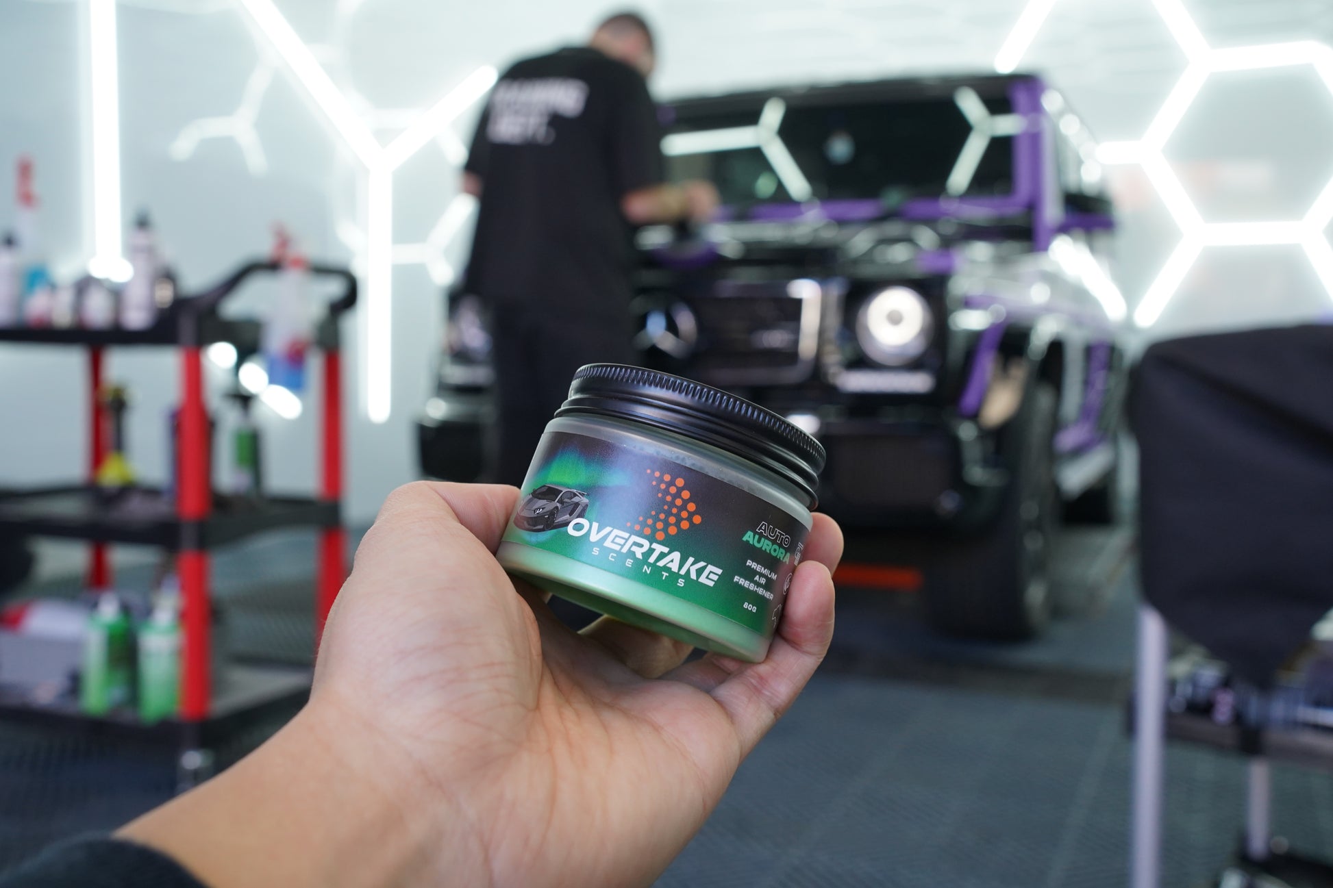 Auto Aurora gel car air freshener held in hand at car detailing studio, large black SUV being detailed in background — Overtake Scents
