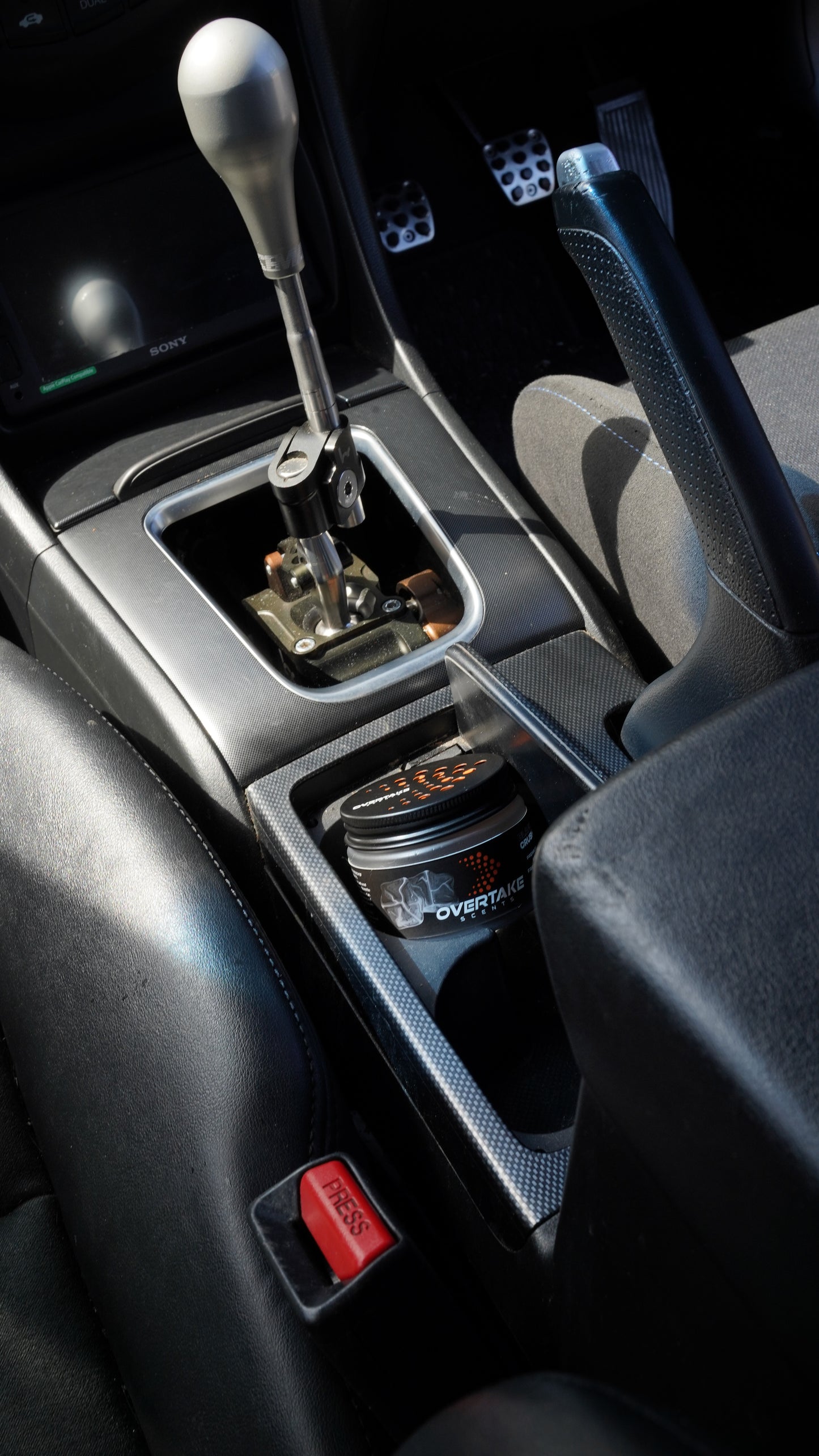 Black Crush gel car air freshener held in hand in front of blue sedan with race number 37 at motorsport event — Overtake Scents