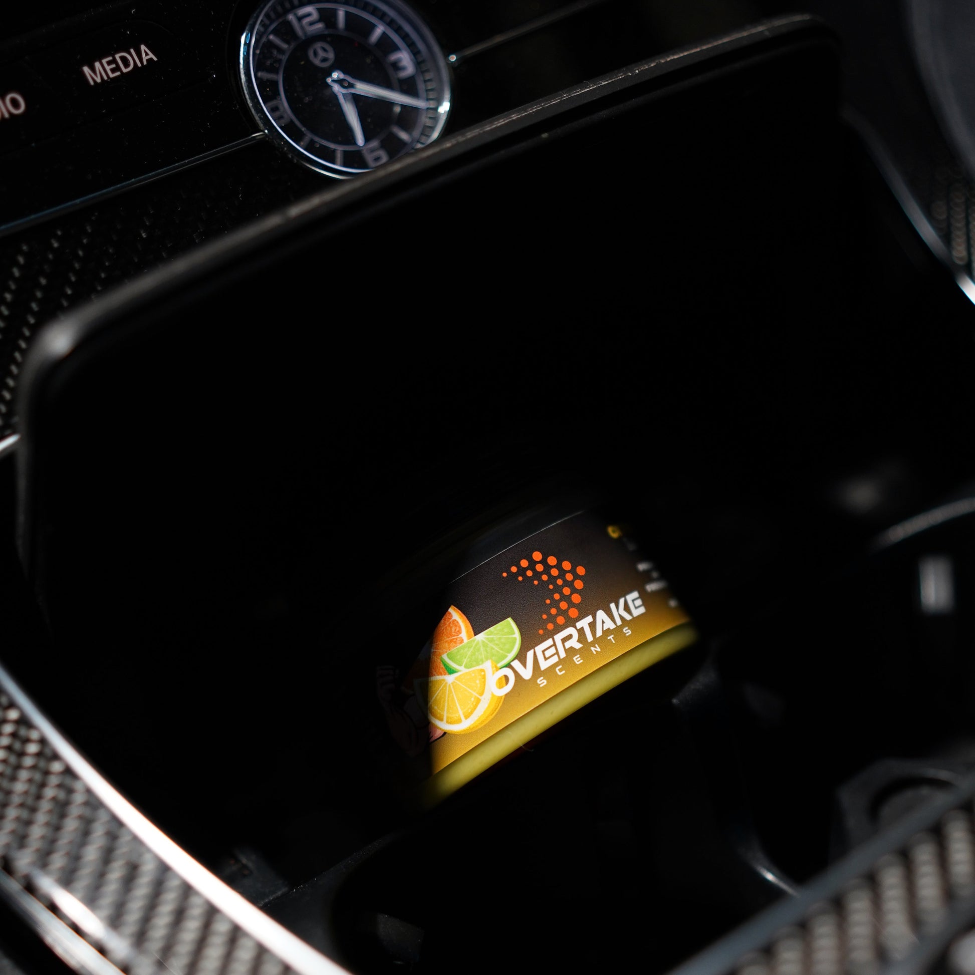Citrus Lift gel car air freshener in Mercedes-Benz center console storage cubby, analog clock and MEDIA button visible — Overtake Scents