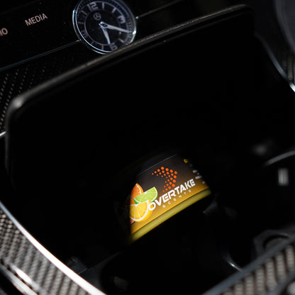 Citrus Lift gel car air freshener in Mercedes-Benz center console storage cubby, analog clock and MEDIA button visible — Overtake Scents