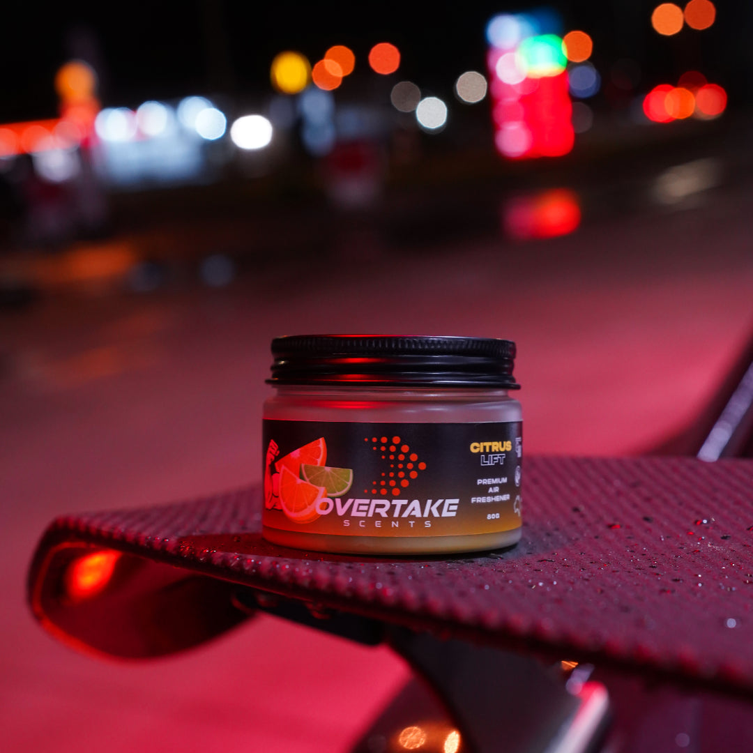 Citrus Lift gel car air freshener on car rear spoiler at night with city lights bokeh — Overtake Scents