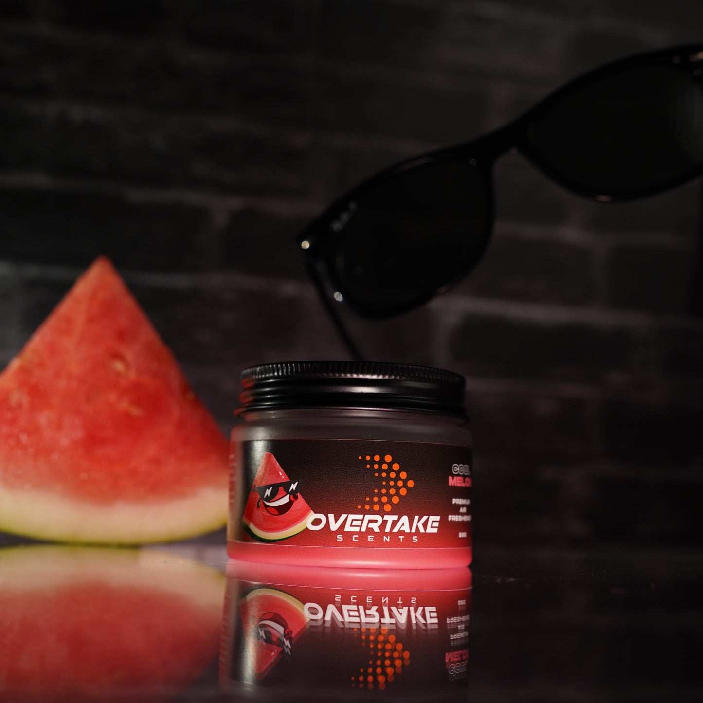 Cool Melon gel car air freshener flat lay with fresh watermelon slice and sunglasses on dark reflective surface — Overtake Scents